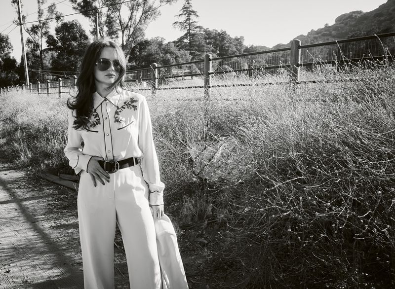 Monochrome portrait of actress Joey King wearing sunglasses and a patterned western shirt standing near a rural wooden fence.