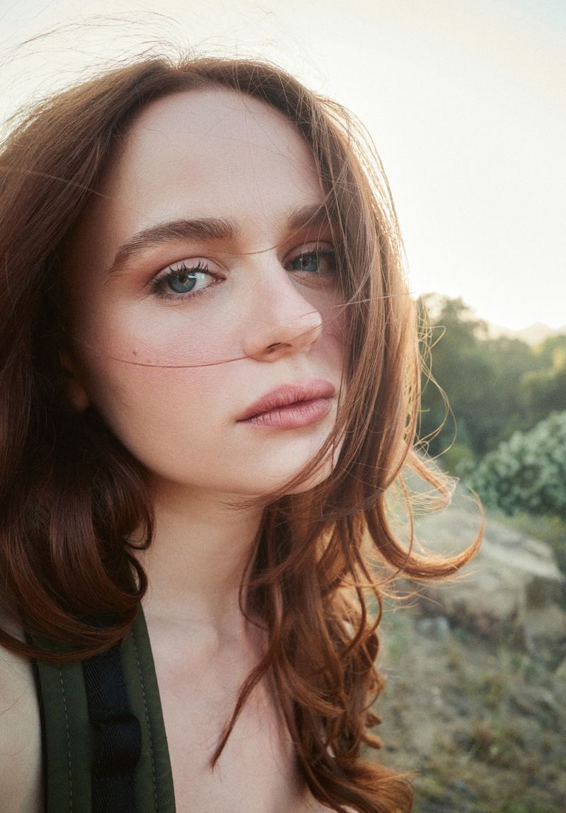 Close-up portrait of actress Joey King outdoors with soft natural lighting and trees in the blurred background.