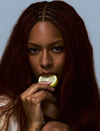 Portrait of Ravyn Lenae holding a lemon slice to her lips for Heroine Magazine