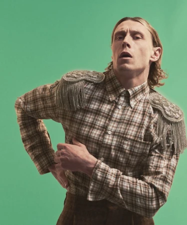 Actor George MacKay in a plaid shirt with embellished epaulets against a green background for HERO Magazine