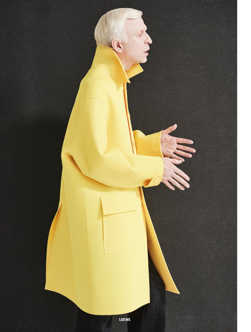Man wearing a bright yellow overcoat with large pockets against a dark textured background for 10 Men Magazine editorial