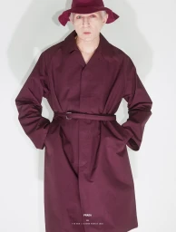 Man wearing burgundy trench coat and matching bucket hat against a plain light wall for 10 Men Magazine editorial