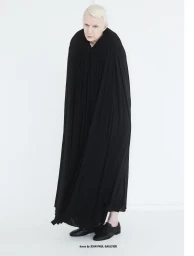 Full-length portrait of a man wearing a long pleated black cloak and black shoes against a white background for 10 Men Magazine.