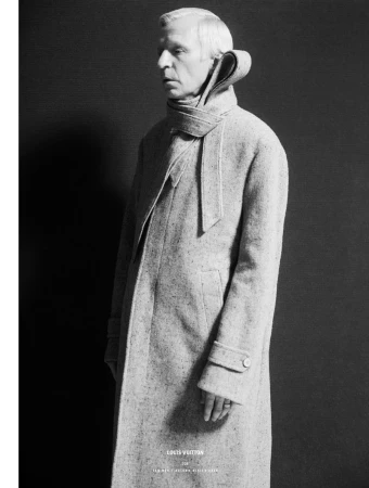 Man wearing a textured grey overcoat with an integrated scarf collar against a dark background