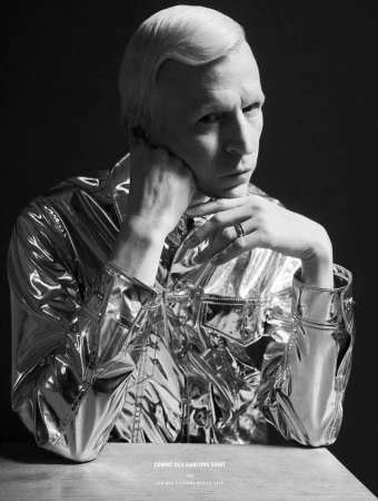 Portrait of Jay Jay Johanson wearing a metallic silver shirt against a dark background for 10 Men Magazine.