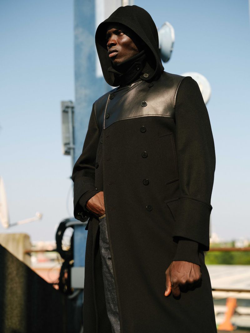 Model Macoumba Lo in a black hooded coat against an outdoor blue sky backdrop for U Repubblica