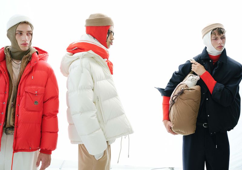 Three male models wearing layered outerwear and beanies against a bright white background