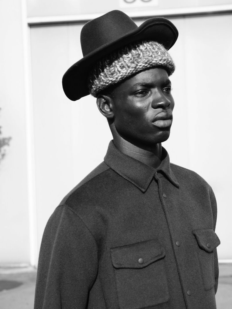 Black man wearing a textured hat and dark shirt against an outdoor wall for U Repubblica project Miles from here