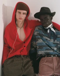 Two male models posing against a white wall for U Repubblica, wearing patterned knitwear and trousers.