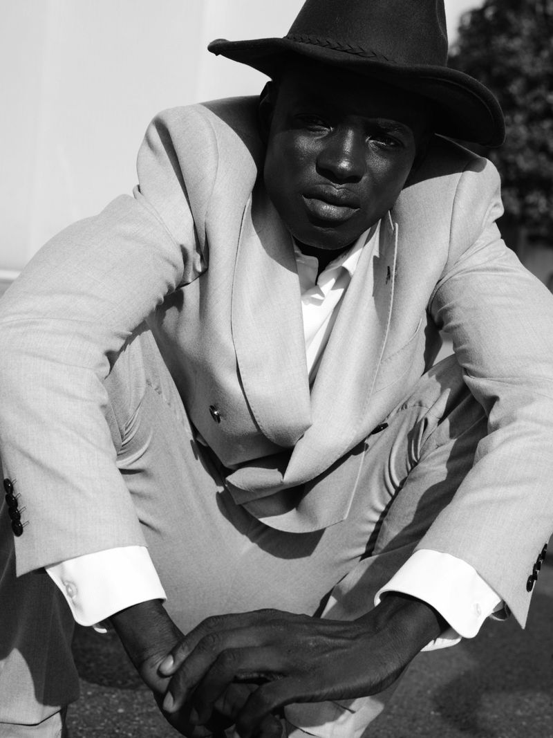 Black man wearing a light-coloured suit and dark fedora crouching outdoors for U Repubblica Miles from here project