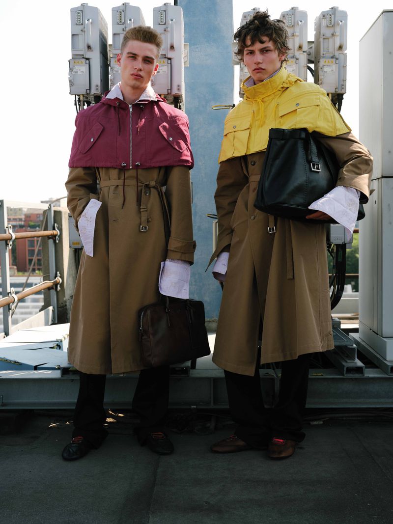 Two male models in long tan coats standing on a rooftop holding bags for U Repubblica Miles from here editorial.