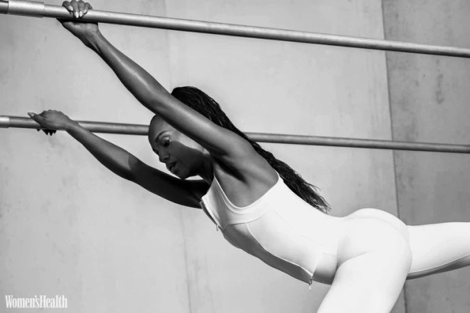 Black and white portrait of Kerry Washington stretching on parallel bars wearing athletic wear