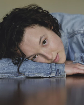 Bella Ramsey wearing a denim jacket resting head on arms for The Guardian portrait