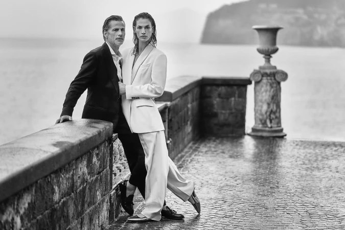 Monochrome fashion shot of a stylish couple posing on a stone balcony overlooking the ocean on an overcast day, Italy.
