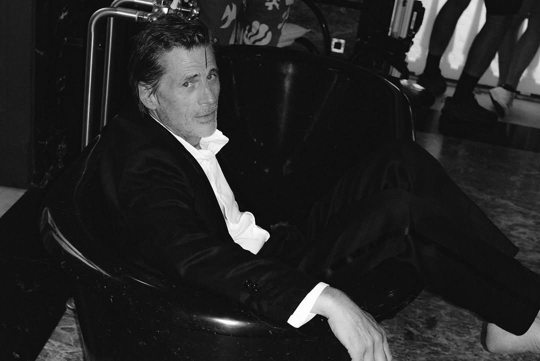 Black and white portrait of a man in a suit, relaxing indoors, looking directly at the camera with a calm expression.