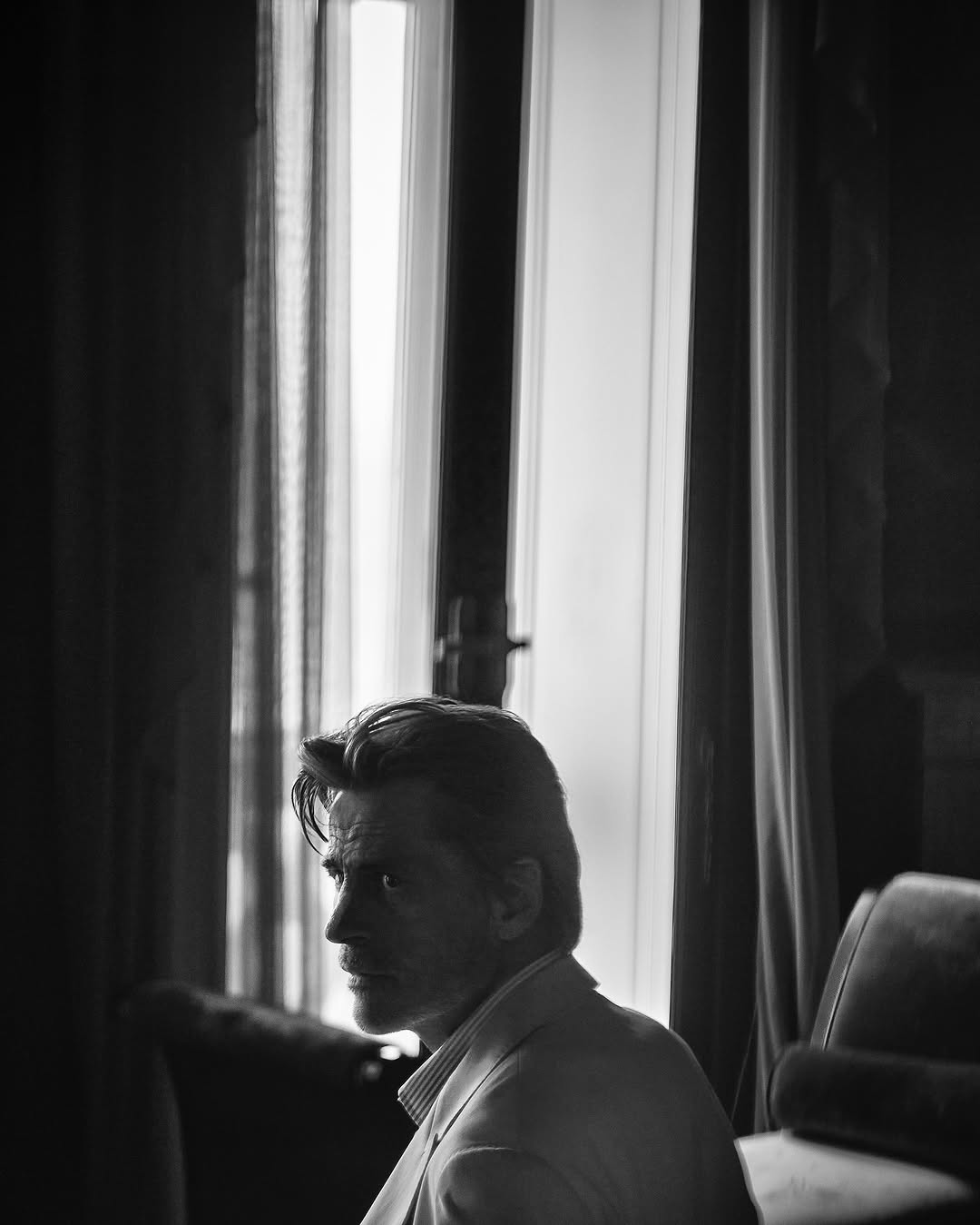 Black and white portrait of a man in a suit jacket. Natural window light illuminates the face in an interior setting.