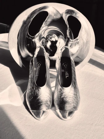 Two metallic silver shoes placed in front of a large, abstract sculptural silver object in a high contrast black and white composition.