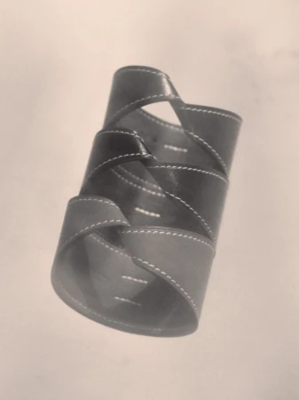 Close up of a dark twisted leather cuff bracelet with white topstitching against a neutral background