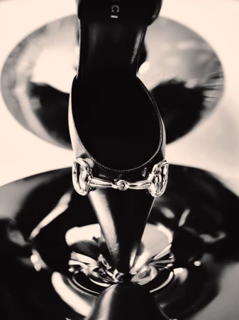 Close-up of a black high-heeled shoe with a metallic horsebit buckle reflected in circular mirrors.