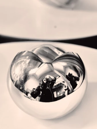 Close-up of a reflective silver metallic sphere showing distorted mirrored reflections of a photographer and interior space.