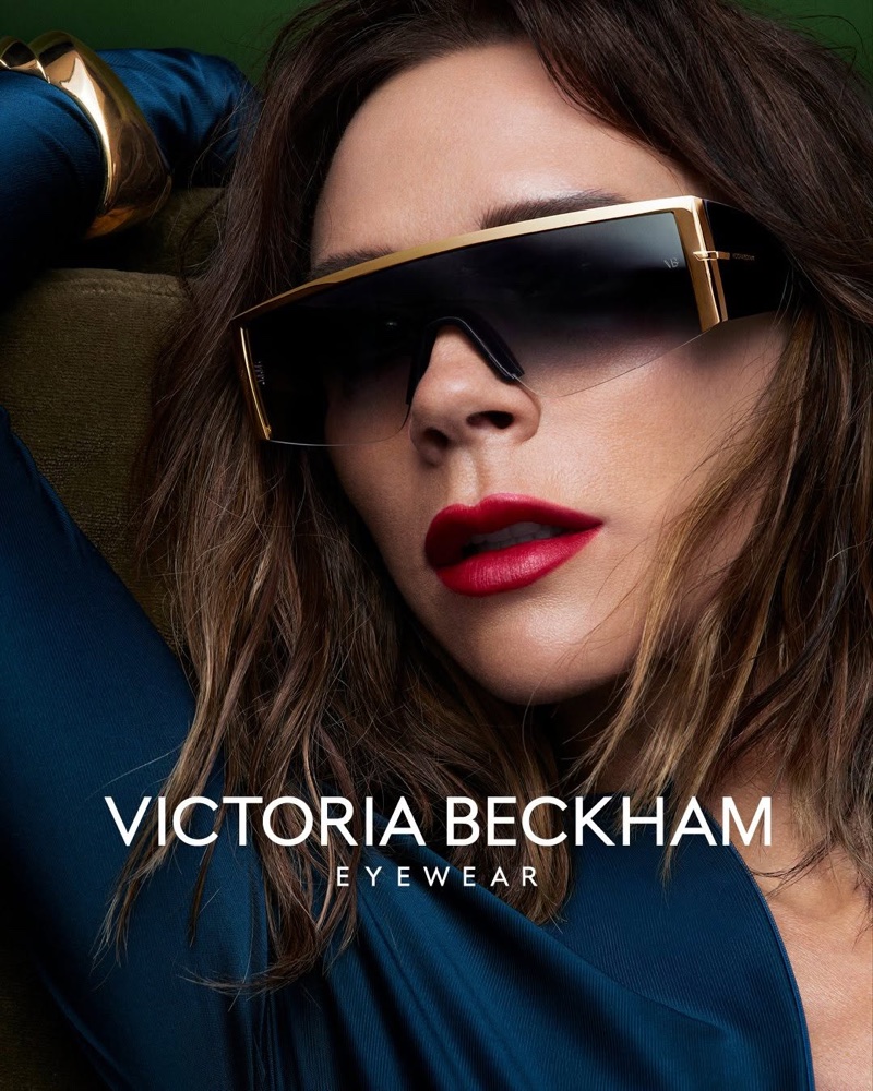 Victoria Beckham wearing oversized gold-rimmed shield sunglasses and a blue top in a Fall-Winter 2026 eyewear campaign portrait.