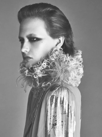 Model in profile wearing a high ruffled collar and patterned top against a neutral studio background