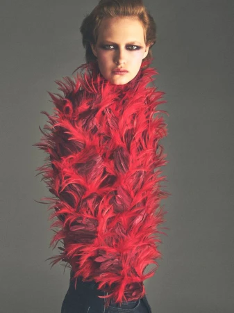 Model wearing a vibrant red feather textured top against a plain grey studio background for Vogue France editorial.