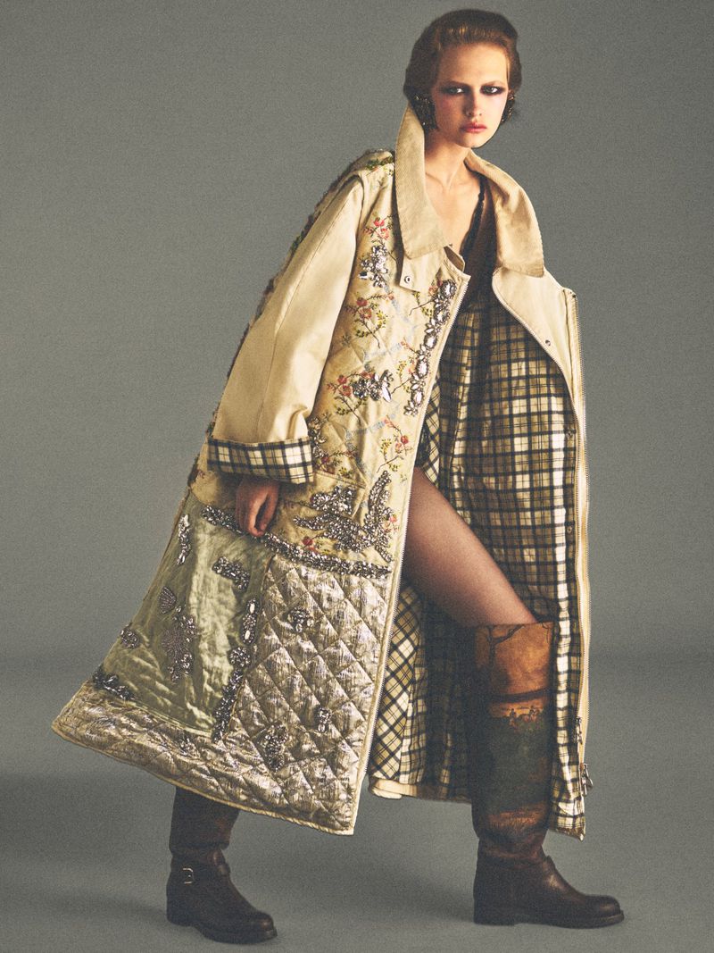 Model wearing an ornate quilted coat and patterned boots against a plain grey studio backdrop