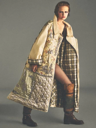 Model wearing an ornate quilted coat and patterned boots against a plain grey studio backdrop