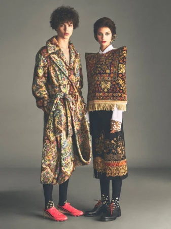 Two models standing against a grey backdrop wearing patterned garments resembling traditional carpets