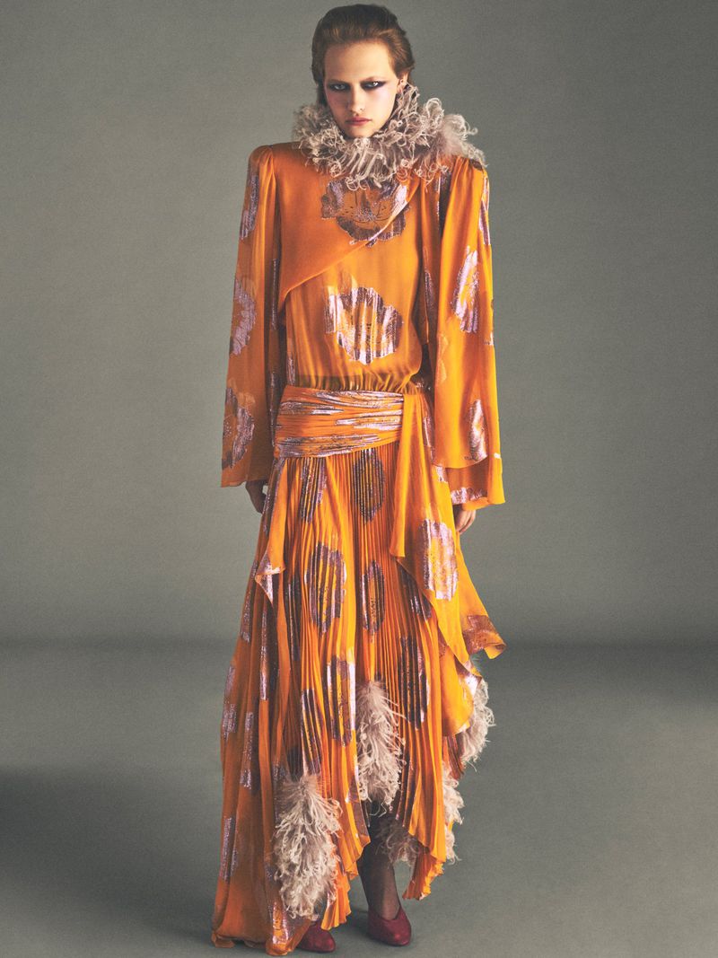 Model in orange patterned dress with ruffled collar standing against grey background for Vogue France editorial