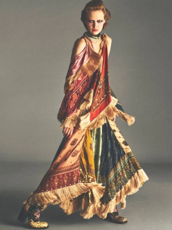 Model in a patterned fringe dress posing against a grey studio background for Vogue France by Allan Hamitouche.