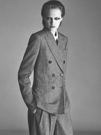 Model in a grey double-breasted suit with dark eye makeup against a plain grey background for Vogue France