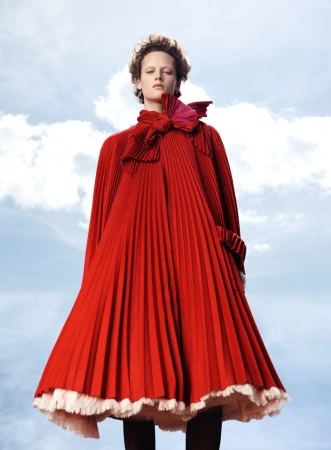 Model wearing a pleated red dress against a cloudy sky background for Vogue France Colorama editorial by Willy Vanderperre.