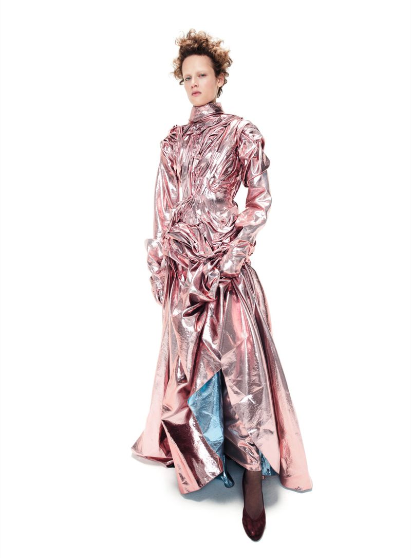Model in metallic pink pleated gown posing against a solid white background for Vogue France