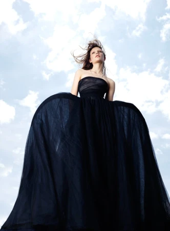 Model in a voluminous black strapless gown photographed against a bright blue sky with clouds in an editorial fashion shot by Willy Vanderperre.