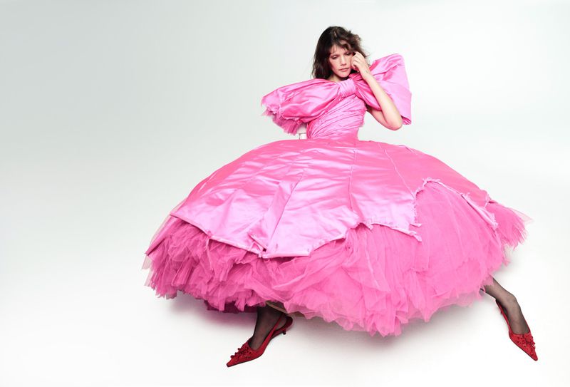Model seated in an oversized bright pink voluminous gown against a white backdrop for Vogue France by Willy Vanderperre.
