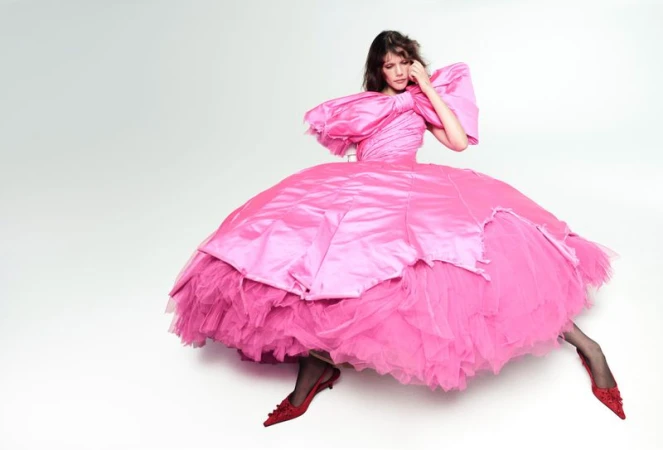 Model seated in an oversized bright pink voluminous gown against a white backdrop for Vogue France by Willy Vanderperre.