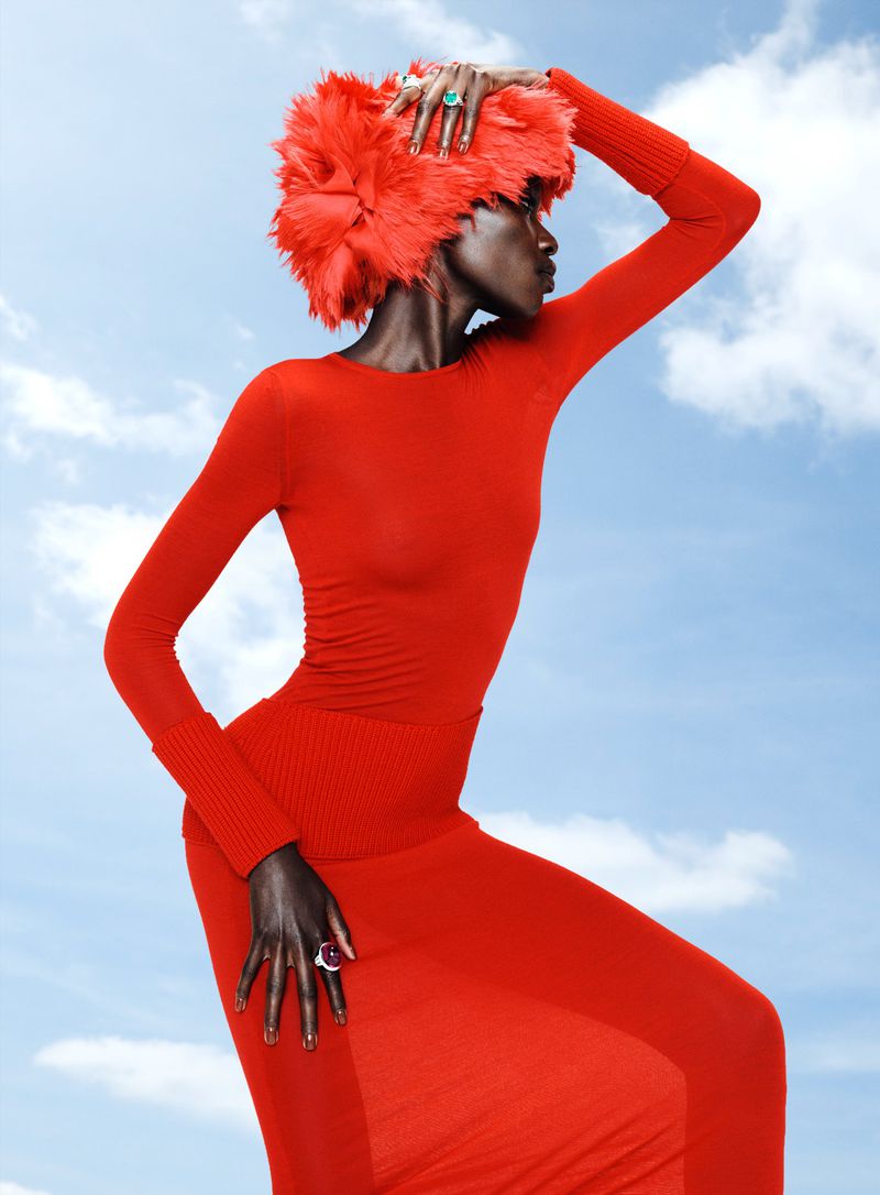 Model in a red dress and fluffy red hat posing against a bright blue sky for Vogue France Colorama editorial