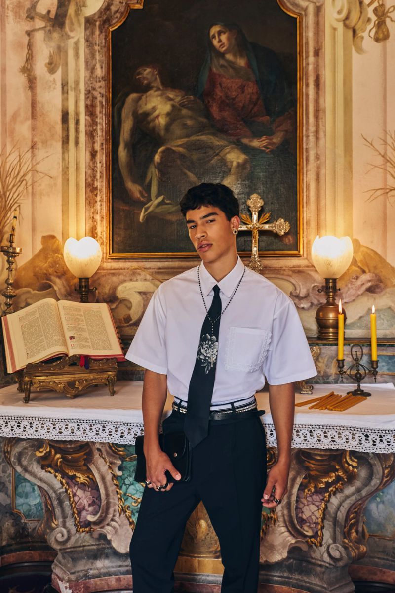Model wearing a white shirt and black trousers with a dark tie standing in front of an altar for Dsquared2 Spring 2027 Menswear.