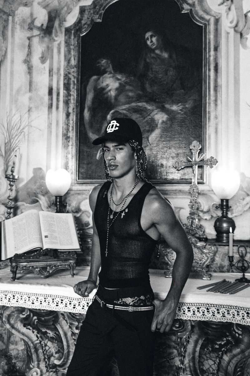 Monochrome fashion portrait of a male model posing inside a classical church interior with religious painting and altar candles.