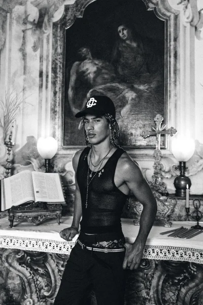 Monochrome fashion portrait of a male model posing inside a classical church interior with religious painting and altar candles.