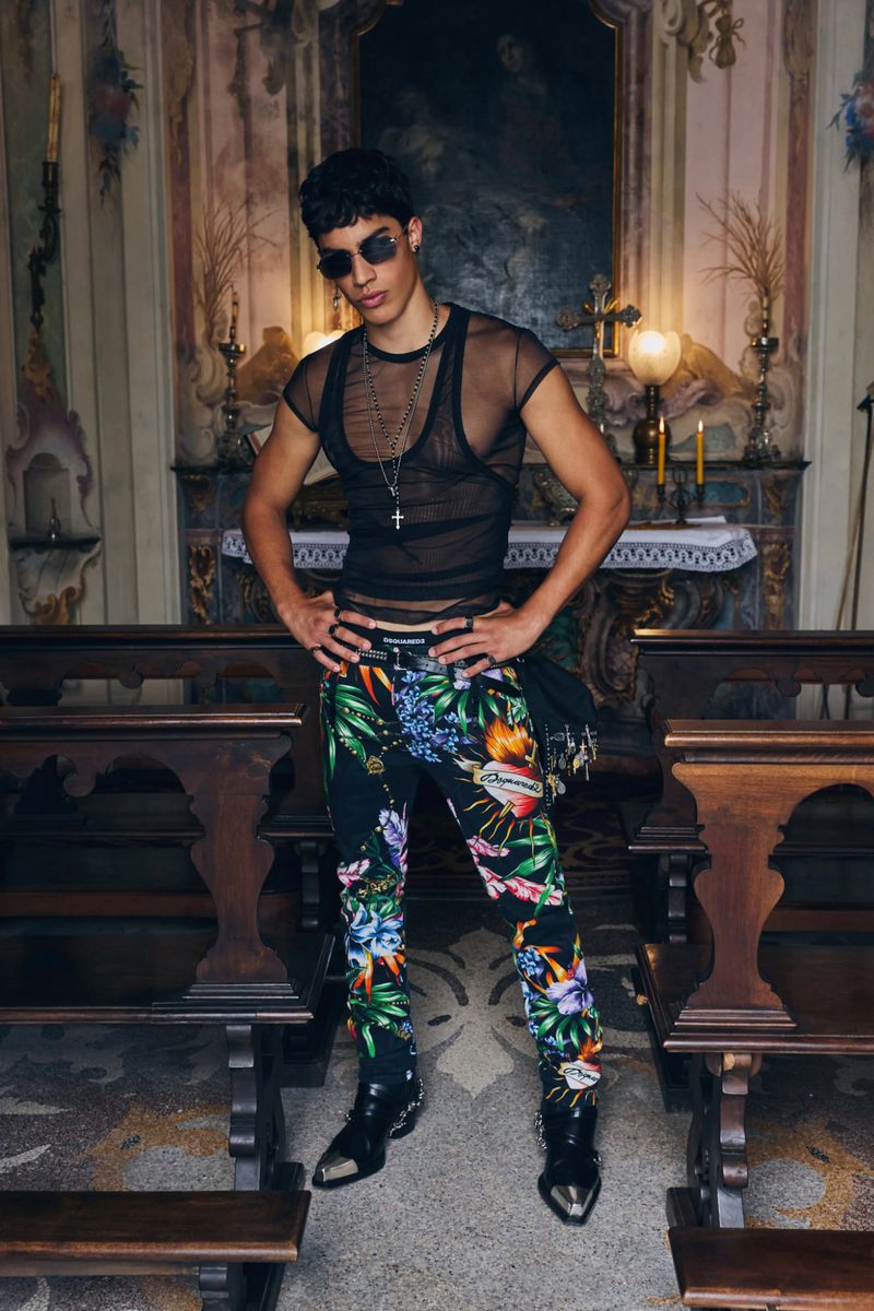 Model wearing dark sunglasses, black mesh top, and floral trousers standing inside a church chapel.