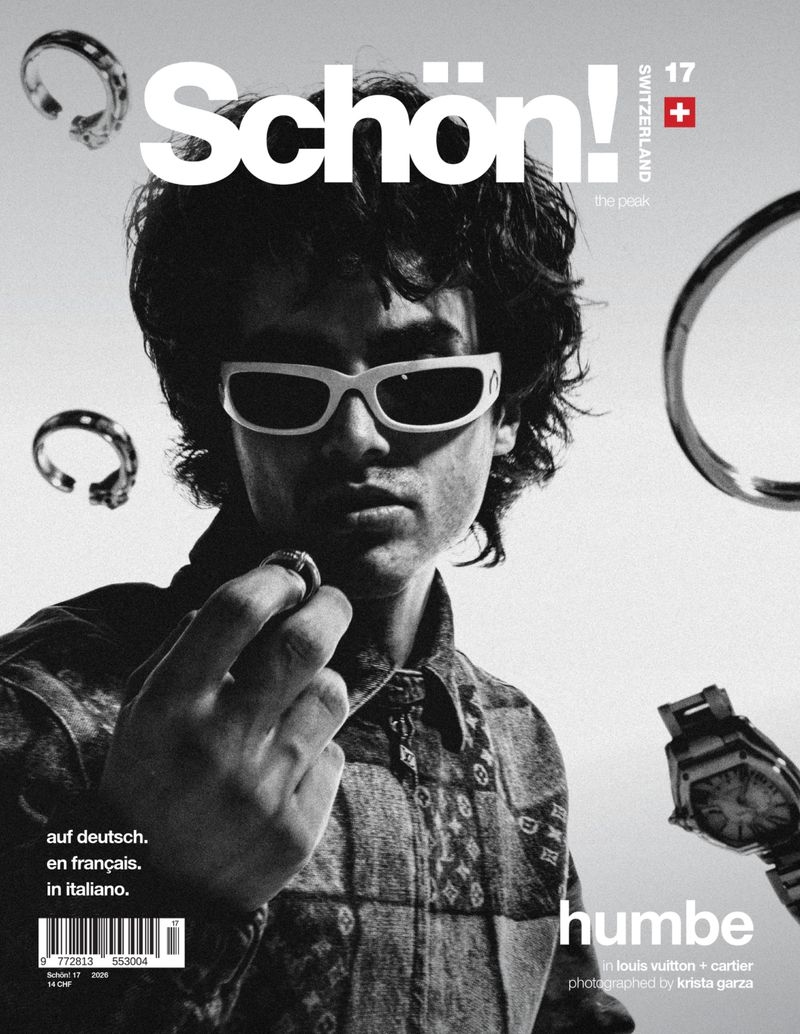 Monochrome magazine cover featuring a male model in white sunglasses holding a ring with floating jewelry around him.
