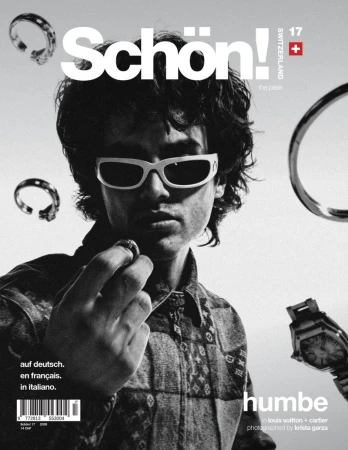 Monochrome magazine cover featuring a male model in white sunglasses holding a ring with floating jewelry around him.
