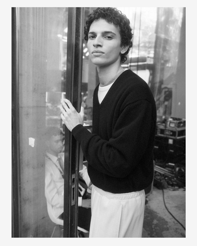 Monochrome portrait of a male model wearing a dark v-neck sweater standing in a doorway