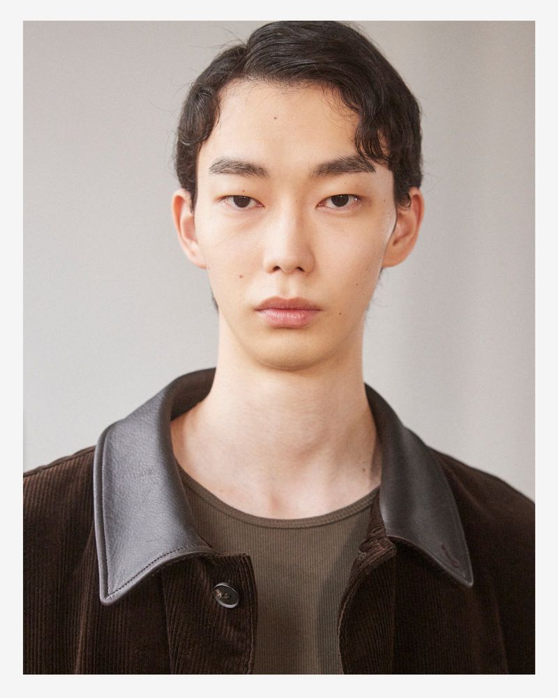 Portrait of a male model wearing a dark brown corduroy jacket with a leather collar against a neutral background.