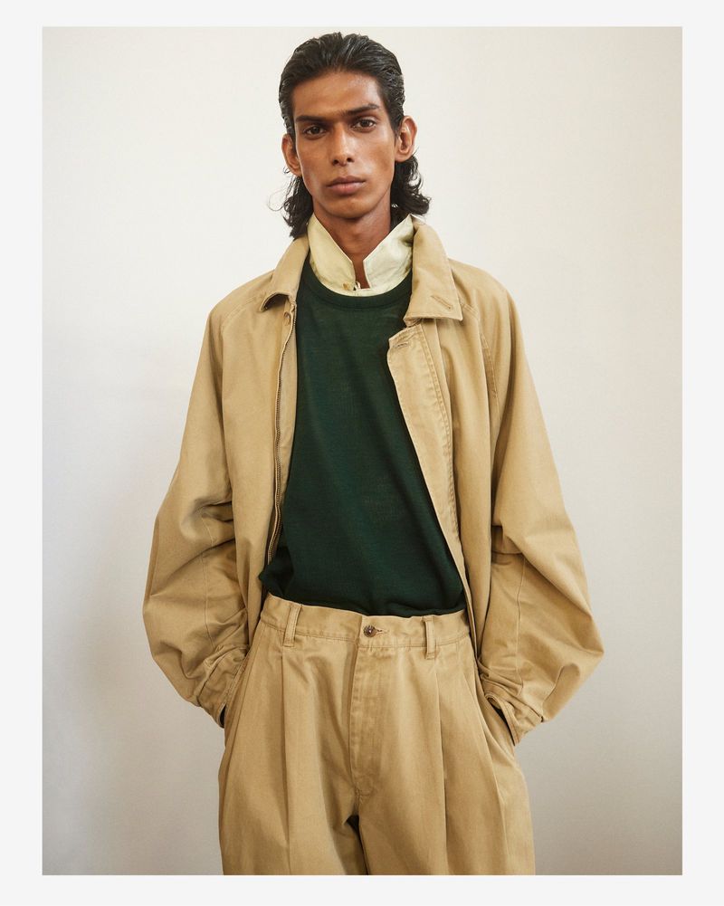 Model wearing a tan jacket, green shirt, and matching trousers against a plain light wall.