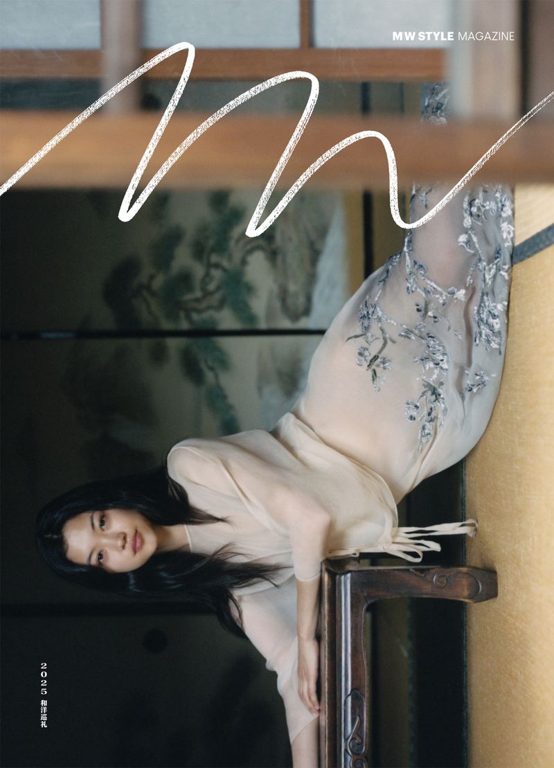 A woman in a sheer gown poses in a magazine cover, leaning on a carved wooden chair against an ornate backdrop with painted details.