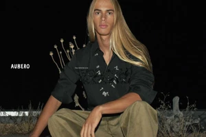 Long-haired male model wearing a black shirt and khaki trousers crouching outdoors at night for Aubero